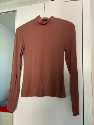 Ljusbrun ribbad turtle neck  - En enkel och stilren ljusbrun turtle neck med lång ärm och ribbad struktur. Toppen har en tight passform och är perfekt att styla med jeans eller kjol. Materialet känns mjukt och stretchigt, vilket gör den bekväm att bära hela dagen.