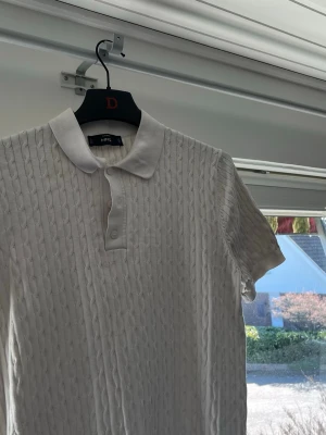 Vit kabelstickad kortärmad skjorta - Vit kabelstickad skjorta med klassisk krage och knappar framtill. Skjortan har korta ärmar och ett snyggt stickat mönster som ger en cool och modern look.