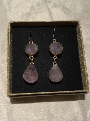 Guldpläterade örhängen med rå ametist  - Örhängen från The moshi. Använda enstaka gång, nu desinficerade i ask. Troligtvis nickelfria eftersom moshis smycken brukar vara det.  Det finns ett litet hack på ett hänge (se bild 3) syns bara på väldigt nära håll, de kom så vid köpet.   Nypris: 150 sek, Pris nu: 80 sek (ask ingår) 
