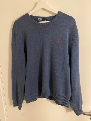 Ralph lauren stickad tröja - Säljer en blå stickad tröja från Polo Ralph Lauren med rund halsringning och det klassiska röda broderade logot på bröstet. Tröjan är i mycket bra skick! Hör av dig om du har några frågor!