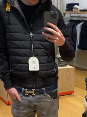 Svart dunväst från Parajumpers - Säljer en svart cardigan från Parajumpers med quiltad design och dragkedja framtill. Västen har en gul detalj vid axeln och två fickor med dragkedja. Perfekt för lager-på-lager och snygg att matcha med jeans. Köpt för 1 månad sen på Johnells för ny pris 4500 säljer den för 3700 utan defekter.