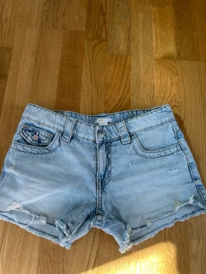 Ljusblå denimshorts med broderade fickor - Gina tricot - Pris kan diskuteras! Snygga ljusblå jeansshorts i denim med slitna detaljer. Baksidan har två fickor med broderade mönster och knappar. Perfekta för sommardagar och enkel att matcha med allt. Kostar 300kr nypris på gina tricot. Säljer för 200kr då de blivit försmå. Använda 1 gång. 