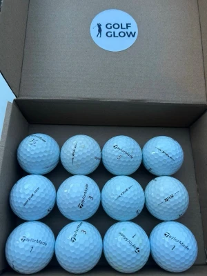 TaylorMade TP5 vita 12-pack  - Säljer ett set med tolv vita golfbollar från TaylorMade, levererade i en kartong märkt Golf Glow. Bollarna har klassisk dimple-yta och är märkta med olika siffror och TaylorMade-loggan. Perfekt för dig som vill fylla på golfbagen inför säsongen.