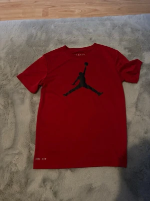 Röd Jordan Dri-Fit t-shirt - Snygg röd t-shirt från Jordan med det klassiska Jumpman-trycket i svart på bröstet. Tillverkad i Dri-Fit-material som andas och håller dig torr. Perfekt för en sportig och avslappnad stil.