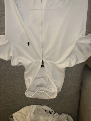 Vit hoodie från Polo Ralph Lauren - Snygg vit hoodie från Polo Ralph Lauren i modellen Custom Fit. Hoodien har dragkedja framtill, huva och den klassiska lilla broderade loggan på bröstet. Perfekt för en clean och stilren look.