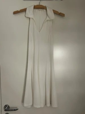 Vit långklänning med krage - Snygg vit långklänning med bred krage och v-ringning. Klänningen har ärmlös design och ett mjukt, lätt tyg som faller fint. Perfekt för dig som gillar minimalistisk och stilren look.