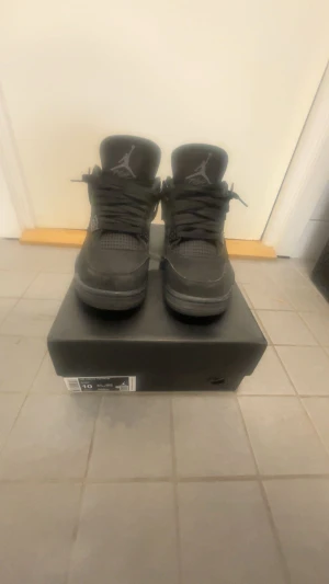Svarta Air Jordan 4 Retro sneakers - Säljer ett par helsvarta Air Jordan 4 Retro sneakers med klassisk mesh och mockadetaljer. Skorna har högt skaft, ikonisk Jumpman-logga på plösen och robust sula. Perfekta för dig som gillar streetwear och vill ha en stilren look.