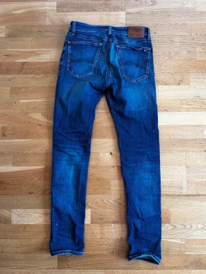 Blå slim fit jeans från Tommy Hilfiger - Snygga blå slim fit jeans från Tommy Hilfiger med klassisk femficksdesign och läderpatch bak i midjan. Jeansen har en lätt tvättad look och raka ben. Perfekta för en trendig och avslappnad stil.