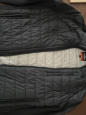 Svart pufferjacka från Parajumpers - Snygg svart pufferjacka från Parajumpers med quiltad design och dragkedjor på fickorna. Jackan har en vit insida och ett broderat märke på ärmen. Perfekt för kalla dagar och har en modern, sportig look.