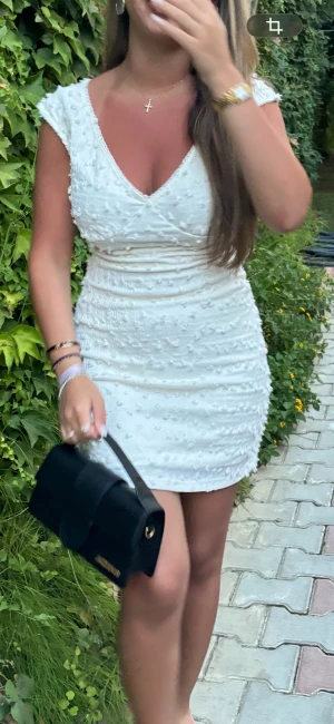 Vit kort klänning med v-ringning - Snygg vit kort klänning med v-ringning och små texturerade detaljer över hela tyget. Klänningen har korta ärmar och figurnära passform, perfekt för dig som vill sticka ut. Materialet känns lätt och bekvämt mot huden.