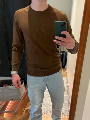 Brun rundhalsad tröja - Säljer en enkel och stilren brun tröja med rund halsringning. Tröjan har långa ärmar och är tillverkad i ett tunt, mjukt material som passar perfekt till jeans. Klassisk passform och ribbade muddar vid ärmslut och nederkant.