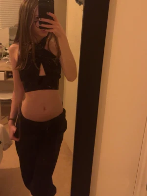 Festlig svart croppad topp - Snygg festlig svart croppad topp med snören som man kan knyta hur man vill. Toppen är ärmlös och har en tight passform som framhäver midjan. Perfekt för dig som vill ha en trendig och stilren look. Toppen har en öppenrygg och skulle säga den passar många storlekar då man kan knyta den själv. På sista bilden så ser man att den är lite nopprig men väldigt lite.