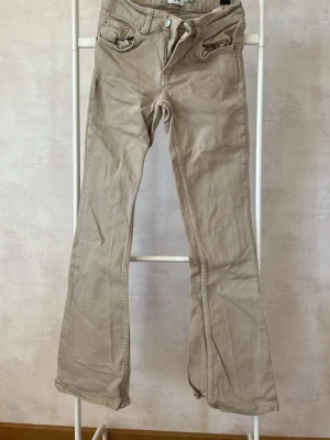 Beige bootcut jeans från Lager 157 - Snygga beige bootcut jeans från Lager 157 med klassiska fem fickor och låg midja. Jeansen har dragkedja och knapp framtill samt Lager-lapp bak i midjan. Tillverkade i mjukt bomullsmaterial med lite stretch för skön passform.
