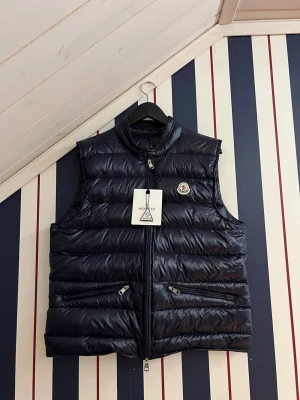 Moncler Gui väst  - Mörkblå Monclerväst som är i storlek 3. Detta motsvarar M-L. Den är extremt bra skick och inte använd mycket, och när den väl användes gjordes den det försiktigt. Både logan och tagen på bild 5 skannar till hemsidan.
