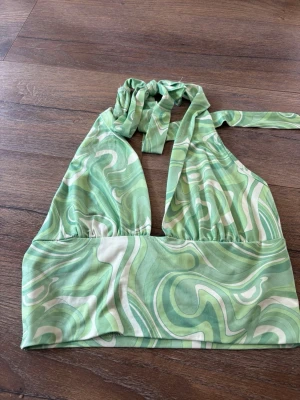 Grön mönstrad halterneck linnetopp - Säljer en grön och vit halterneck linnetopp med swirl-mönster. Toppen har knyt i nacken och är ärmlös, perfekt för varma dagar eller fester.