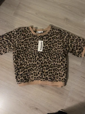 Leopardmönstrad stickad tröja Kappahl - Stickad tröja från Kappahl med leopardmönster i beige, svart och brunt. Tröjan har rund halsringning och ribbade muddar vid ärmslut och nederkant. Perfekt för dig som vill ha en trendig och djurinspirerad look. Helt ny, nypris 399kr. 