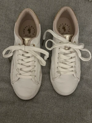 Vita sneakers från Polo Ralph Lauren - Stilrena vita sneakers från Polo Ralph Lauren med gulddetaljer, använts få gånger 