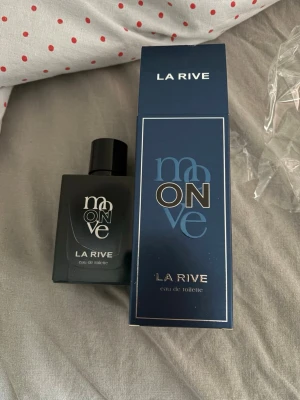 La Rive Moon On Eau de Toilette - La Rive Moon On Eau de Toilette kommer i en stilren, mörkblå och svart fyrkantig flaska med matchande kartong. Flaskan har en modern design med tydlig logga och svart kork. Perfekt för dig som gillar eleganta och minimalistiska parfymer.