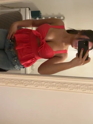 Röd Zara topp  med knyt - Säljer en röd topp med volangkant och knyt framtill. Toppen är ärmlös med smala axelband och har en croppad passform. Perfekt för dig som vill ha en söt och trendig look.