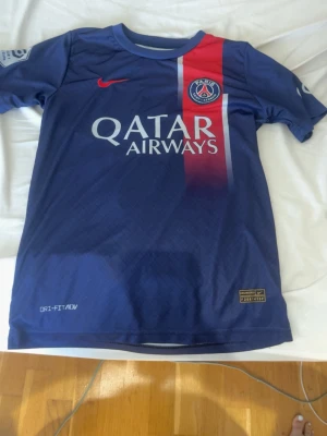 PSG Neymar Jr matchtröja blå Nike - Snygg blå PSG matchtröja från Nike med Neymar Jr och nummer 10 på ryggen. Tröjan har Qatar Airways-tryck på bröstet, röd och vit rand samt PSG-logga. Tillverkad i lätt och ventilerande Dri-FIT material, perfekt för fotboll eller träning.