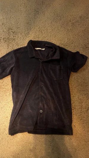 Mörkblå frottéskjorta från 157 - Mjuk och skön mörkblå skjorta från 157 i frottématerial. Skjortan har korta ärmar, klassisk krage, bröstficka och knappar framtill. Perfekt för en avslappnad och chill stil.