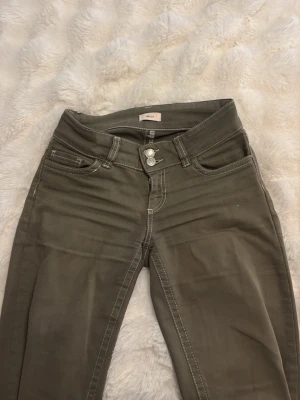 Olivgröna jeans från NELLY - Snygga olivgröna jeans från NELLY med raka ben och vita kontrastsömmar. Jeansen har dubbla knappar i midjan, klassiska fem fickor och coola broderade detaljer på bakfickorna. Perfekta för en trendig och avslappnad stil. 