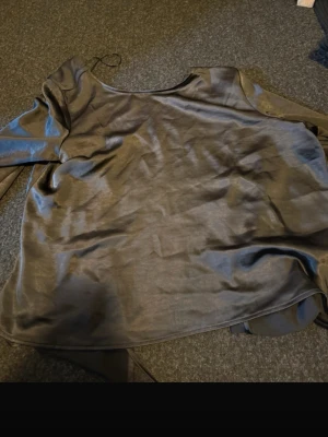 Mörkgrå satinblus med knytband - Snygg mörkgrå blus i glansigt satintyg med långa ärmar och rund halsringning. Blusen har dekorativa knytband i sidan som ger en trendig look. Perfekt för dig som gillar stilrena och moderna plagg.