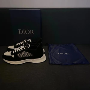 Svarta och vita sneakers - Snygga sneakers i svart och vitt med klassiskt mönster på sidan. Skorna har vit snörning, rund tå och platt sula. Ovandelen kombinerar textil och mockadetaljer för en exklusiv känsla. Perfekta för dig som vill sticka ut med stil.