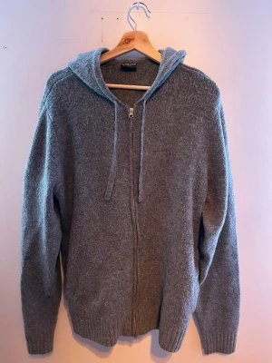 Grå hoodie med dragkedja från Firefly - Mysig grå hoodie från Firefly i storlek L. Tillverkad i mjukt stickat material, har dragkedja framtill, två fickor och justerbar huva med snören. Perfekt för chill dagar och enkel att matcha med jeans eller joggers.