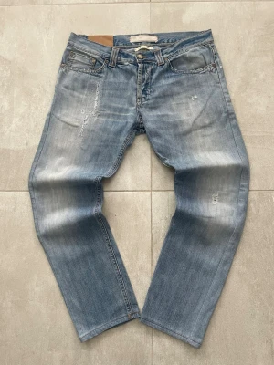 Blå slitna jeans från Dondup limited edition red selvedge premium - Säljer ett par blå jeans från Diesel med slitningar och tvättade detaljer. Jeansen har klassisk femficksmodell, knappgylf och en avslappnad passform. Materialet är denim i bomull och färgen är ljusblå med slitna partier och whiskers.  Mått 📏 Totallängd: 93cm Midjelängd: 42 Innersömmlängd: 71 Lårviddlängd: 28 Skador 🔧: Litet skador på båda bakfickor, sömmar som är lite slitna och tvättade.  Storlek 🧍: W32 (Står 34, men passar som W32)  Passform: Regular/Slim    