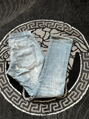 Ljusblå slitna jeans med patchar - Säljer ett par ljusblå jeans med raka ben och flera slitningar samt patchade detaljer framtill. Jeansen har klassisk femficksmodell och normal midja. Perfekta för en avslappnad och trendig look. Materialet är denim i bomull.
