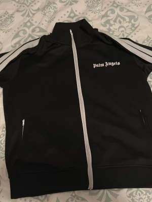 Palm Angels Kofta - Storlek M. Dragkedjan på vänster sidan är dock fast, man kan inte dra ner den. Även 2-3 små hål på den vita sträckan vid armarna alltså inte in i tröjan men det syns knappast.