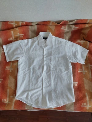 Vit kortärmad skjorta Atlant - Lätt och luftig vit kortärmad skjorta från Atlant i syntetiskt material, perfekt för sommaren. Lös / boxy passform, snygg som streetwear eller mer formell om den stoppas in i byxor.