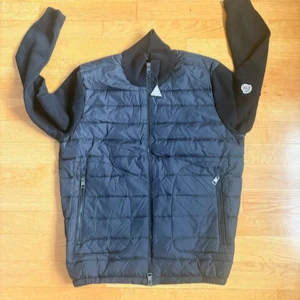 Svart cardiganjacka från Moncler - Snygg svart cardiganjacka från Moncler med quiltad framsida och mjuka stickade ärmar och rygg. Jackan har dragkedja framtill, två fickor med dragkedja och en liten Moncler-logga på ärmen. Perfekt för lager-på-lager och streetstyle.