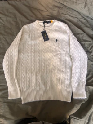 Vit kabelstickad tröja Polo Ralph Lauren - Kabelstickad vit tröja från Polo Ralph Lauren i storlek M (Passar även storlek S). Aldrig använd då den är för liten. Skriv om du har några frågor!