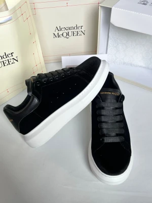 Svarta Alexander McQueen sneakers - Stilrena svarta sneakers från Alexander McQueen med tjock vit sula och guldfärgad logga på plösen. Skorna har en klassisk låg silhuett, svarta skosnören och ovandel i mocka och läder. Perfekta för dig som vill ha en clean och lyxig look.