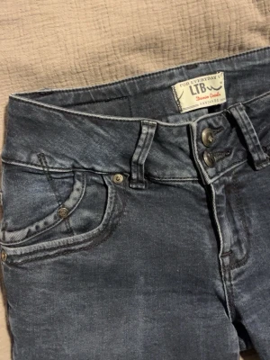 Mörkblå jeans från LTB - Säljer ett par mörkblå jeans från LTB med dubbla knappar i midjan och klassisk femficksdesign. Jeansen har en lätt tvättad look och smal passform som sitter snyggt längs benen. Perfekta för dig som gillar en stilren och modern look. W27, L32