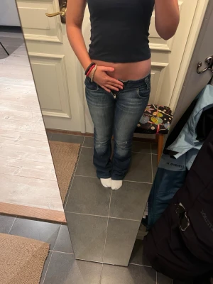 Blå bootcut jeans från Lee - Säljer ett par blå bootcut jeans från Lee med snygga slitningar och klassisk femficksmodell. Jeansen har låg midja, dragkedja och knapp framtill samt Lee-lapp bak i midjan. Tillverkade i denim med lätt stretch för skön passform.