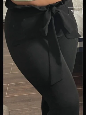 Svarta leggings med midjeband - Snygga svarta leggings med hög midja och volangkant upptill. Midjebandet knyts i en stor rosett framtill vilket ger en extra detalj. Stretchigt material som sitter tight och bekvämt. Perfekta till crop tops eller oversized tröjor.