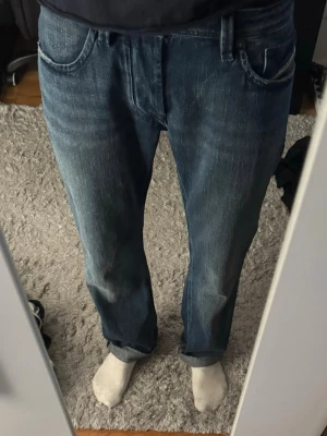 Blå raka jeans med vintage-look - Säljer ett par blå jeans med rak passform och klassisk femficksdesign. Jeansen har en snygg tvättad vintage-look och är tillverkade i denim. Perfekta för en avslappnad och stilren outfit.