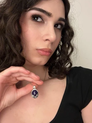 Katherine Pierce halsband and armband - Snyggt halsband i silver med en stor, oval lila sten som hängsmycke. Hänget har detaljerade silverinfattningar runt stenen som ger ett unikt och elegant intryck. Perfekt för dig som vill ha något som sticker ut och kompletterar din stil.