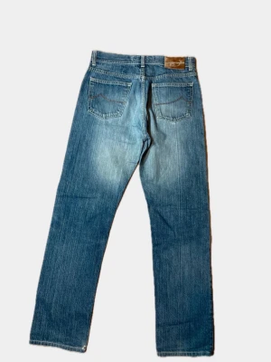 Jacob Cohen - Klassiska blå jeans från Jacob Cohen med rak passform och fem fickor. Jeansen har en snygg tvättad look med ljusare partier och detaljerad söm på bakfickorna. Tillverkade i slitstark denim.        102 cm långa.                                                                  37 cm waist