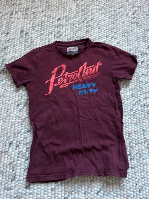 Vinröd t-shirt från Petrol Ind. - Säljer en vinröd t-shirt från Petrol Industries med trycket 'Petrol Ind. Heavy Duty' i rött och blått framtill. Klassisk passform med korta ärmar och rund hals. Perfekt för dig som gillar streetwear och vill ha en cool vardagslook.