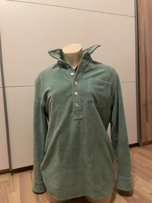 Grön frotté henley från nikben  - Säljer en grön henley-skjorta i mjuk frotté med lång ärm och bröstficka. Skjortan har flera knappar framtill och en avslappnad passform. Perfekt för dig som gillar en chill och bekväm stil.