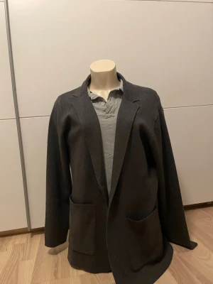 Mörkgrå  kavaj - Stilren mörkgrå kavaj med avslappnad, oversized passform och två stora framfickor. Klassisk krage och enkel design utan synliga knappar. Perfekt för en trendig och avslappnad look.