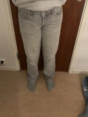 Ljusgrå raka jeans - Säljer ett par ljusgrå jeans med rak passform och klassisk femficksdesign. Jeansen har normal midja och stängs med knapp och dragkedja. Perfekta till en avslappnad stil och passar till det mesta. Materialet är mjukt denim i bomull. (lite slitna) passar tjejer som e 165. storlek XS å S