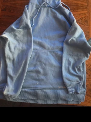 Ljusblå hoodie från SELFMADE - Snygg ljusblå hoodie från SELFMADE med klassisk känguruficka och ribbade muddar. Hoodien har dragsko i huvan och diskret logga nere vid midjan. Perfekt för en chill och avslappnad stil.