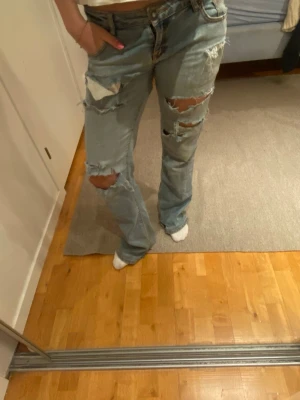 Ljusblå håliga jeans - Säljer ett par ljusblå jeans med raka ben och stora slitningar och hål på både fram- och baksida. Jeansen har en avslappnad passform och klassisk femficksdesign. Perfekta för en trendig och avslappnad stil. De är köpa secondhand i Holland, står ej storlek eller märke men unika och snygga jeans som passar från XXS-M
