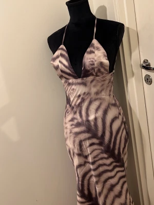 Zebramönstrad långklänning med smala band - Säljer en snygg långklänning med zebramönster i beige och svart. Klänningen har smala axelband, djup urringning och figurnära passform. Materialet är glansigt och känns lyxigt, perfekt för dig som vill sticka ut. 🤍🩶