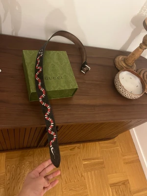 Gucci svart bälte med orm-motiv - Säljer ett svart bälte från Gucci i skinn med ett coolt orm-motiv i rött, vitt och svart längs hela bältet. Spännet är i silverfärg och bältet har en exklusiv känsla. Perfekt för dig som vill sticka ut med en unik accessoar. Kvitto box dustbag tillkommer i köpet‼️Skriv gärna inte om ni inte är intresserade tack.⚠️